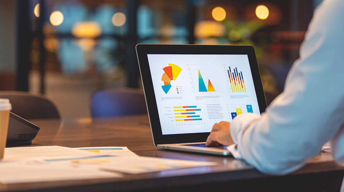 A person in an office looks at laptop with charts on the screen.