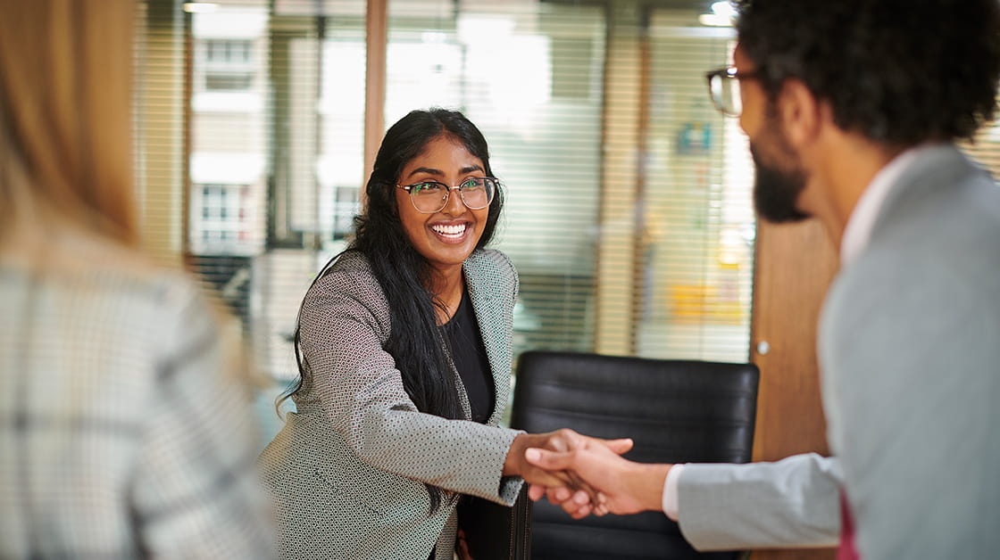 A smiling young professional woman shakes hands with a professional man.
