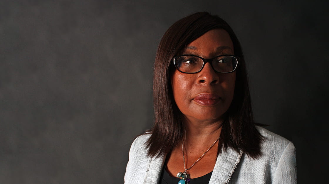 Judge Carol Taylor is a Black-Caribbean woman, wearing glasses and a pale grey suit. She has a neutral expression and is looking left away from the camera.