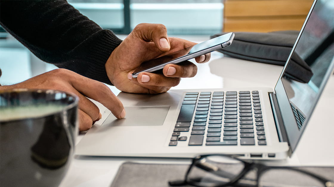 Man using laptop and smartphone to produce report