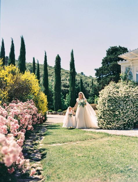A bride walks through a beautiful garden whilst holding hands with her bridesmaid
