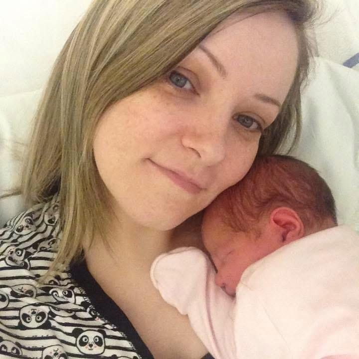 Claire Liddy in a black and white stripy top top holding a her newborn daughter. Claire smiles at the camera with the baby on her shoulder. Claire has blonde hair.