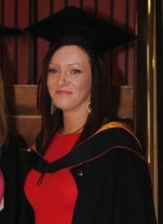 Claire Liddy smiles on her LLB graduation day she has straight brown hair and is wearing a red dress along with a graduation cap and gown.