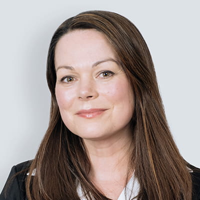 Helen is a woman with brown hair, she is wearing a suit and smiles into the camera. 