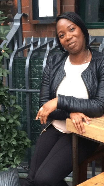 Lara is a woman with short black hair, she is sitting outdoors, smiling into the camera. 