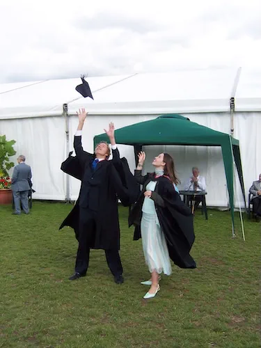 Rosie Burbidge and another student, standing outside, throwing their graduation caps in the air.