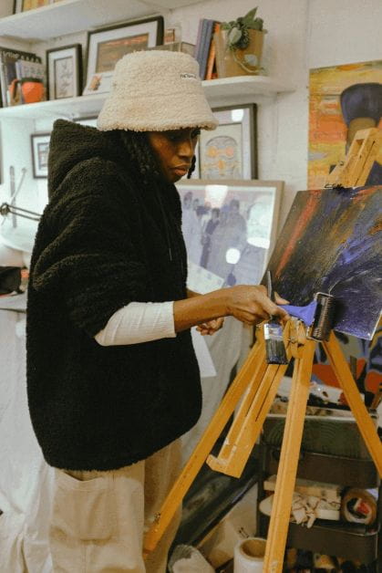 Salome Coker stands at an easel creating an artwork with a roller.