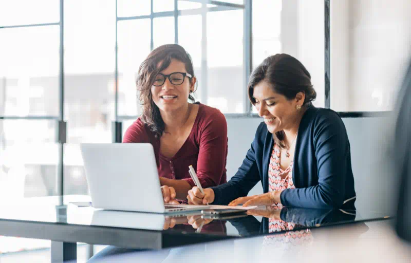Two smiling solicitors sit together at a desk talking